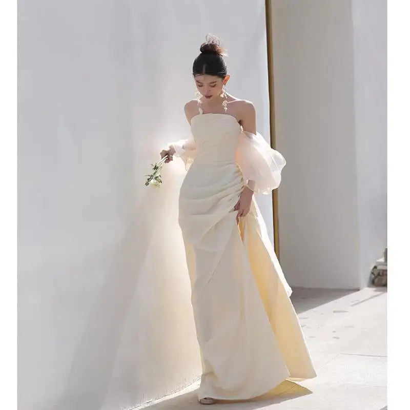 A flowing off-the-shoulder ivory satin outdoor travel shooting light yarn gown with voluminous sheer puff sleeves and draped bodice