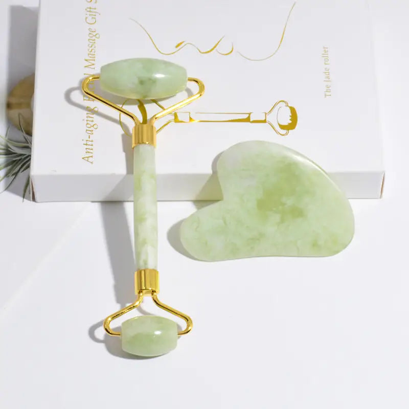 A pale green jade rolling and gua sha gift set with gold-toned handles and branded packaging