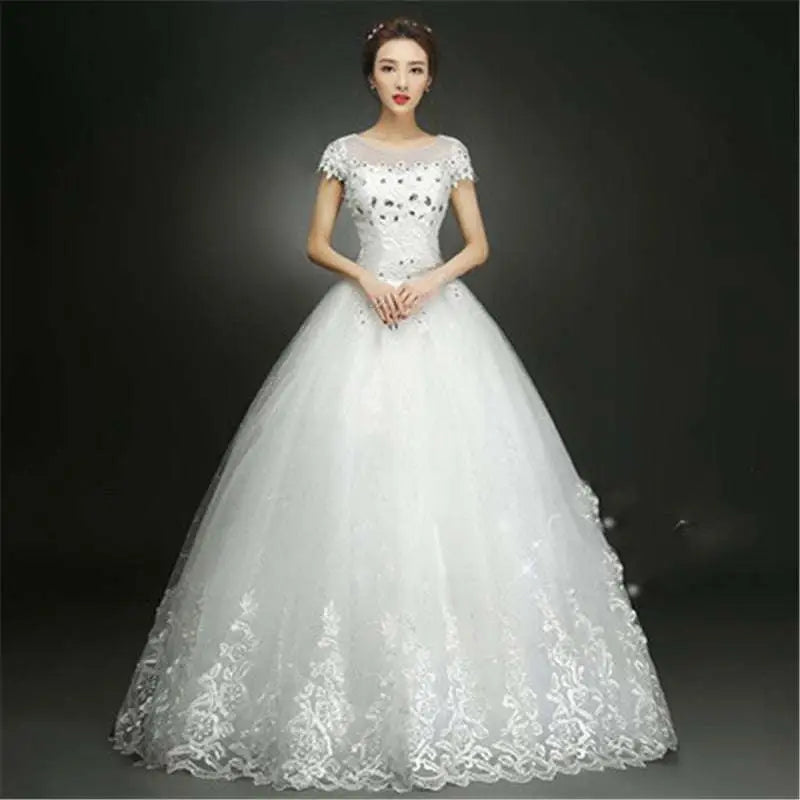 White beaded floor length wedding dress with a fitted bodice, short sleeves, and intricate lace detailing on tulle skirt hem