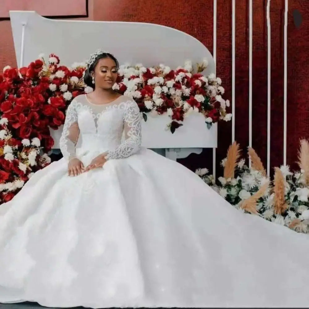 A woman in a white lace ball gown wedding dress with long sleeves and off the shoulder neckline sits gracefully