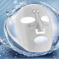 A white silicone electric facial massage mask with a playful face design and intricate swirling lace pattern