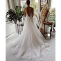 A flowing white wedding gown featuring lace strap backless design with deep back cutout and delicate beading details