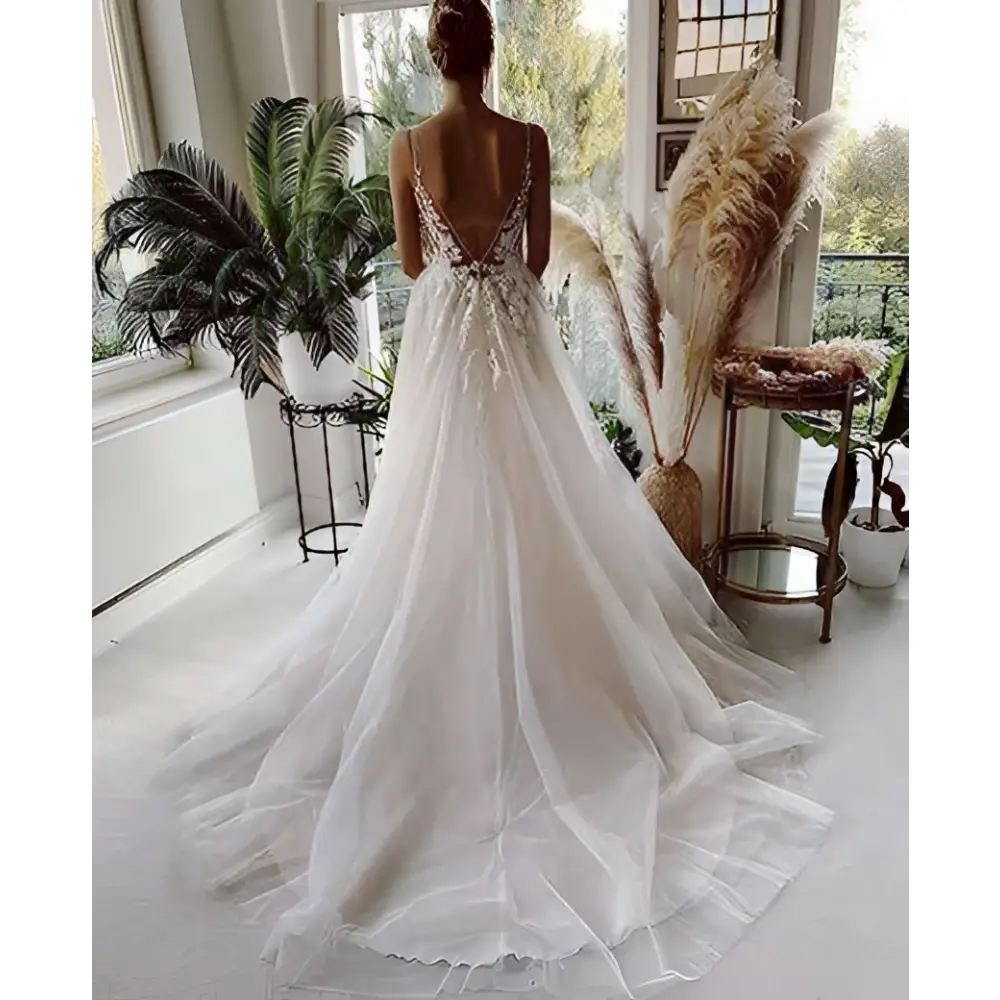 A flowing white wedding gown featuring lace strap backless design with deep back cutout and delicate beading details