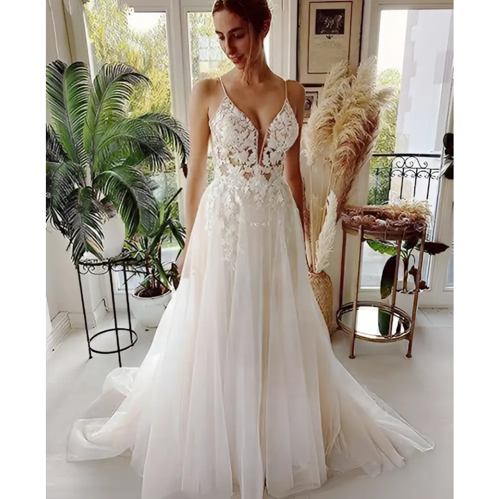 A flowing white wedding gown featuring lace strap backless design with intricate lace detailing and a deep v neckline