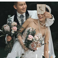 The bride wears a sheer white lace wedding dress with intricate floral appliqués for a summer couple photo shoot