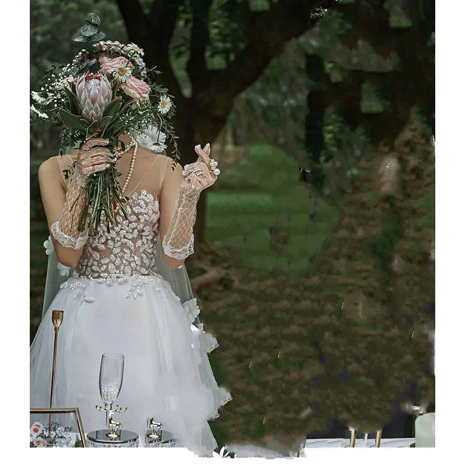 A bride wearing an elegant white lace wedding dress with sheer veil and beaded gloves in a summer couple photo shoot