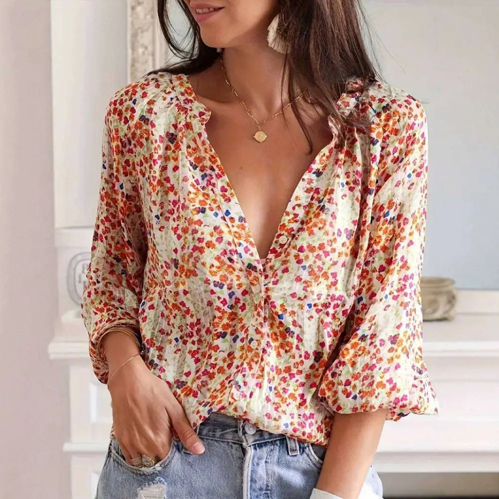 A woman wears a cream-colored lantern sleeve floral print v neck blouse with vibrant orange red and blue patterns