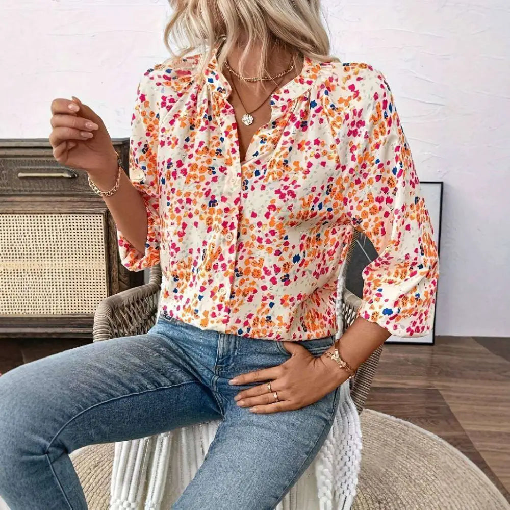 A woman wears a cream-colored lantern sleeve floral print v neck blouse with vibrant orange pink and blue patterns