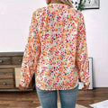 A woman wears a cream-colored lantern sleeve floral print v neck blouse with vibrant orange pink and blue flowers