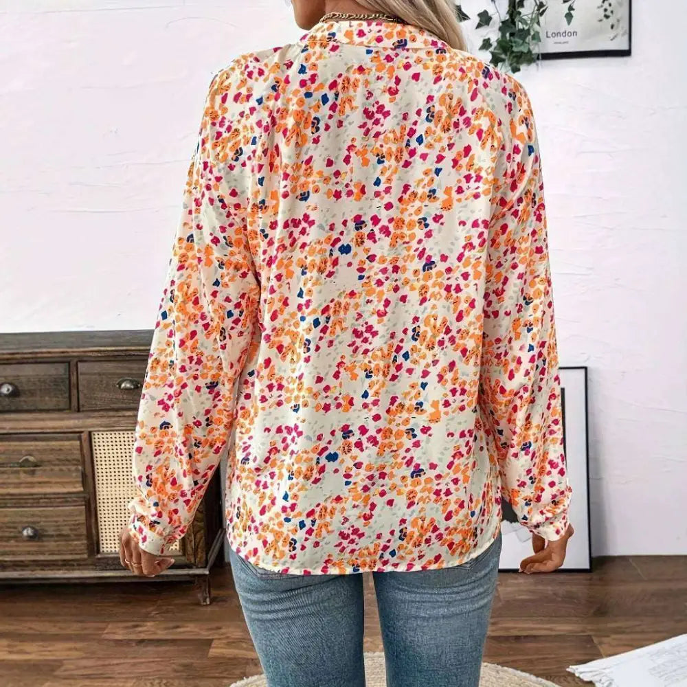 A woman wears a cream-colored lantern sleeve floral print v neck blouse with vibrant orange pink and blue flowers