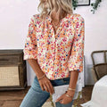 A woman wearing a cream-colored lantern sleeve floral print v neck blouse with vibrant pink orange and blue flowers