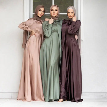 Three women wearing large hem satin long sleeve abayas in dusty rose sage green and deep burgundy colors