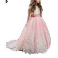 A young girl wears a pink and white lace wedding dress with lavender tulle lace and an embellished satin sash