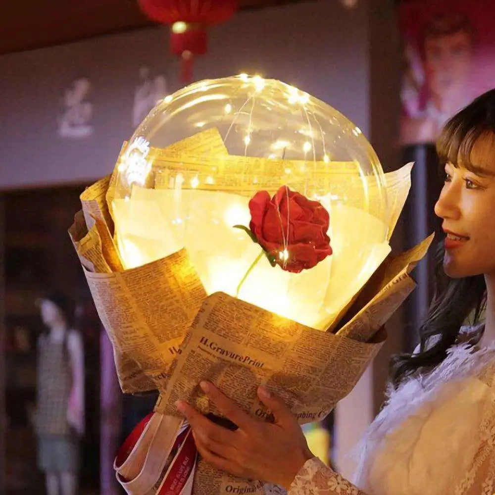 A single red luminous balloon rose encased in a transparent bobo ball illuminated with warm fairy lights wrapped in newspaper