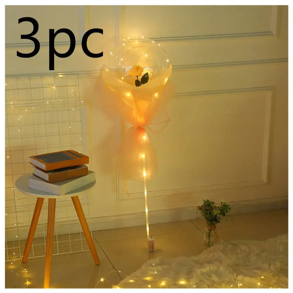A clear transparent bobo ball luminous balloon rose bouquet with a single yellow rose and warm string lights