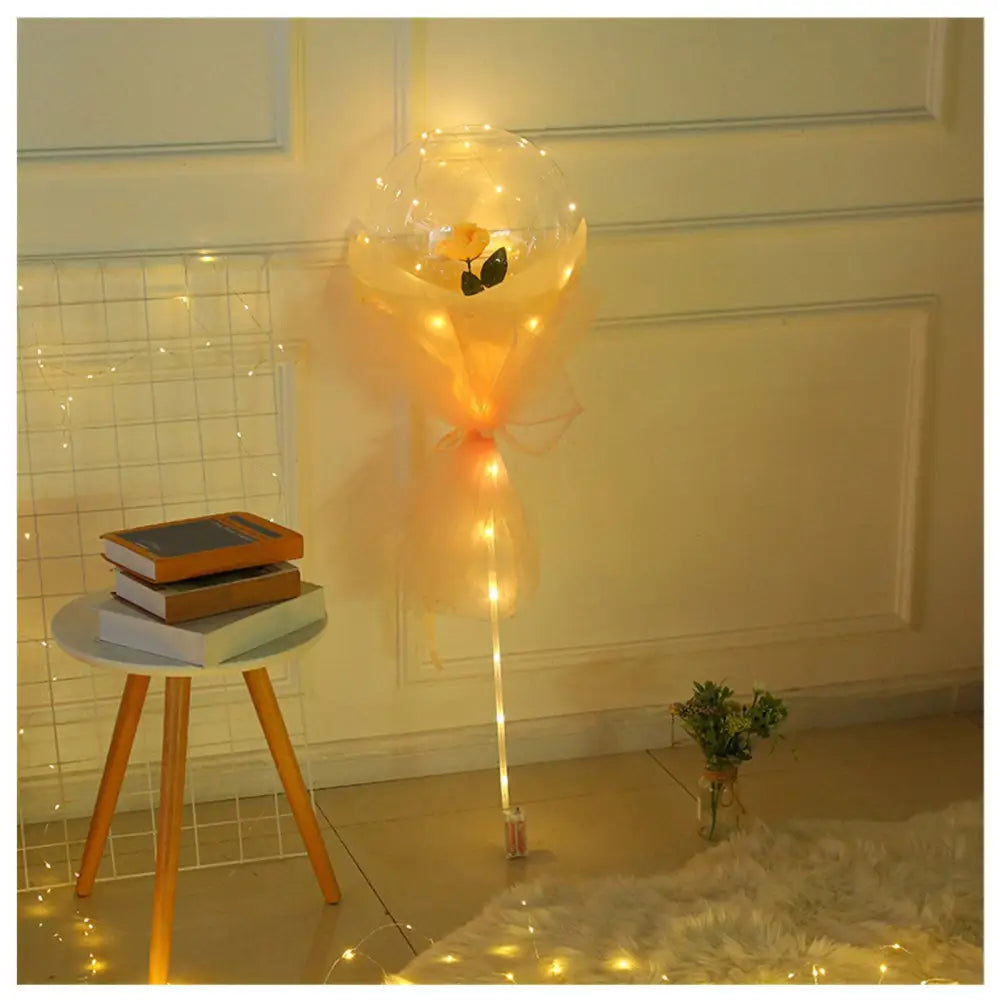 A luminous balloon rose bouquet featuring a glowing transparent bobo ball with a yellow rose and peach organza wrap
