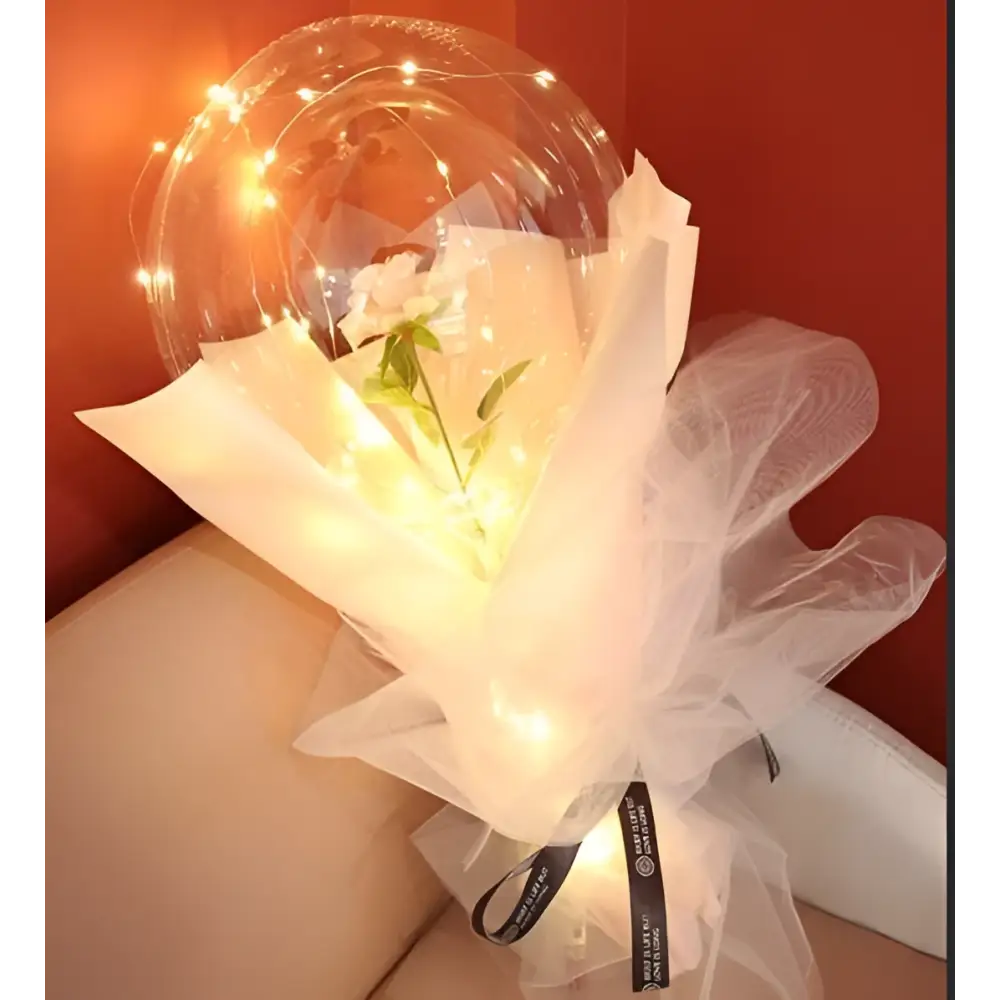 A delicate white flower inside a transparent bobo ball luminous balloon rose wrapped in sheer tulle with warm lights