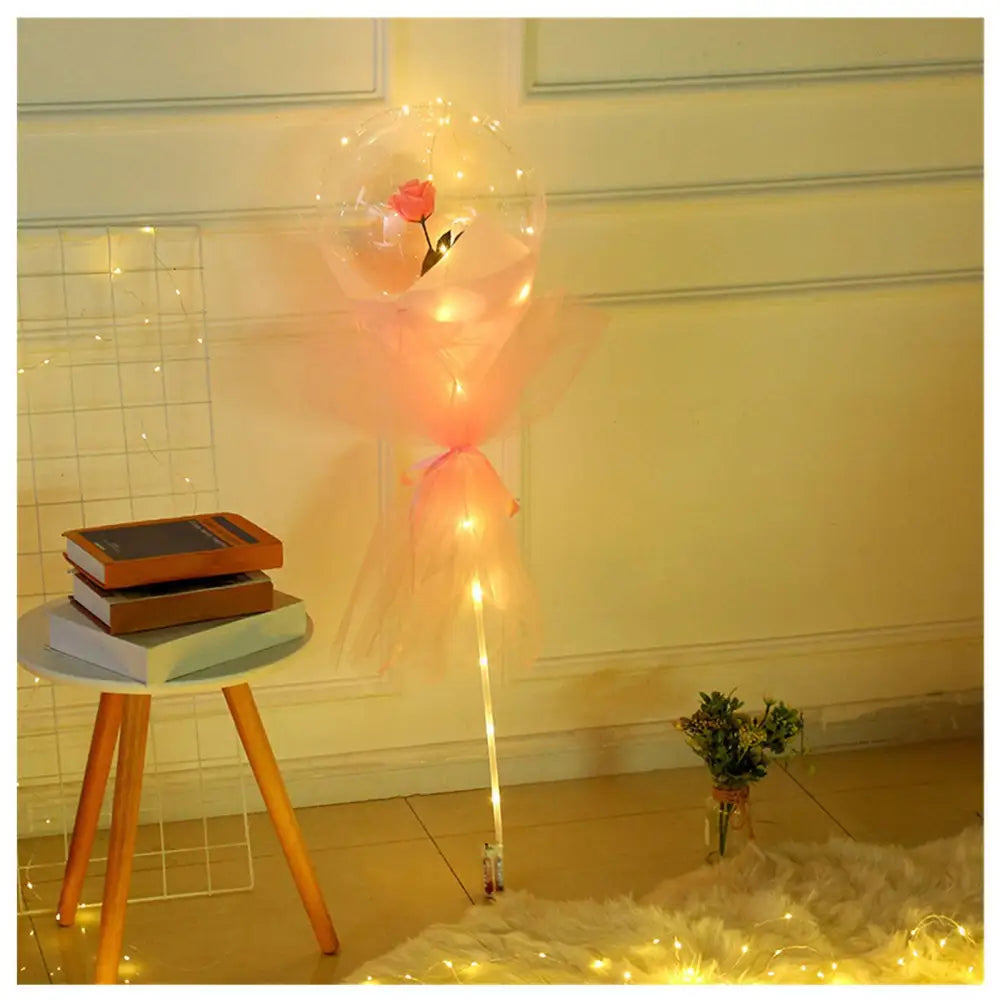 A luminous balloon rose bouquet with a pink rose inside a transparent bobo ball wrapped in peach tulle and warm lights