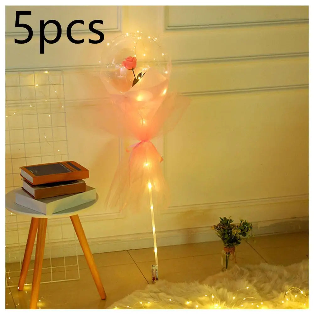 A luminous balloon rose bouquet featuring a single pink rose inside a transparent bobo ball wrapped in peach organza with string lights