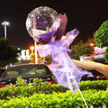 A clear transparent bobo ball luminous balloon rose bouquet featuring a single purple rose wrapped in lavender organza and dark purple paper