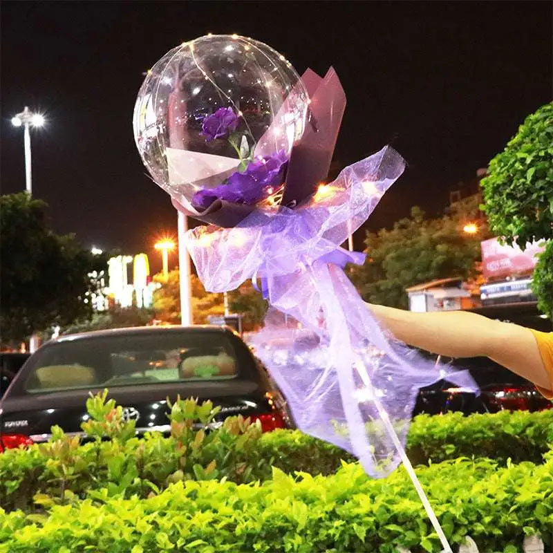 A clear transparent bobo ball luminous balloon rose bouquet featuring a single purple rose wrapped in lavender organza and dark purple paper
