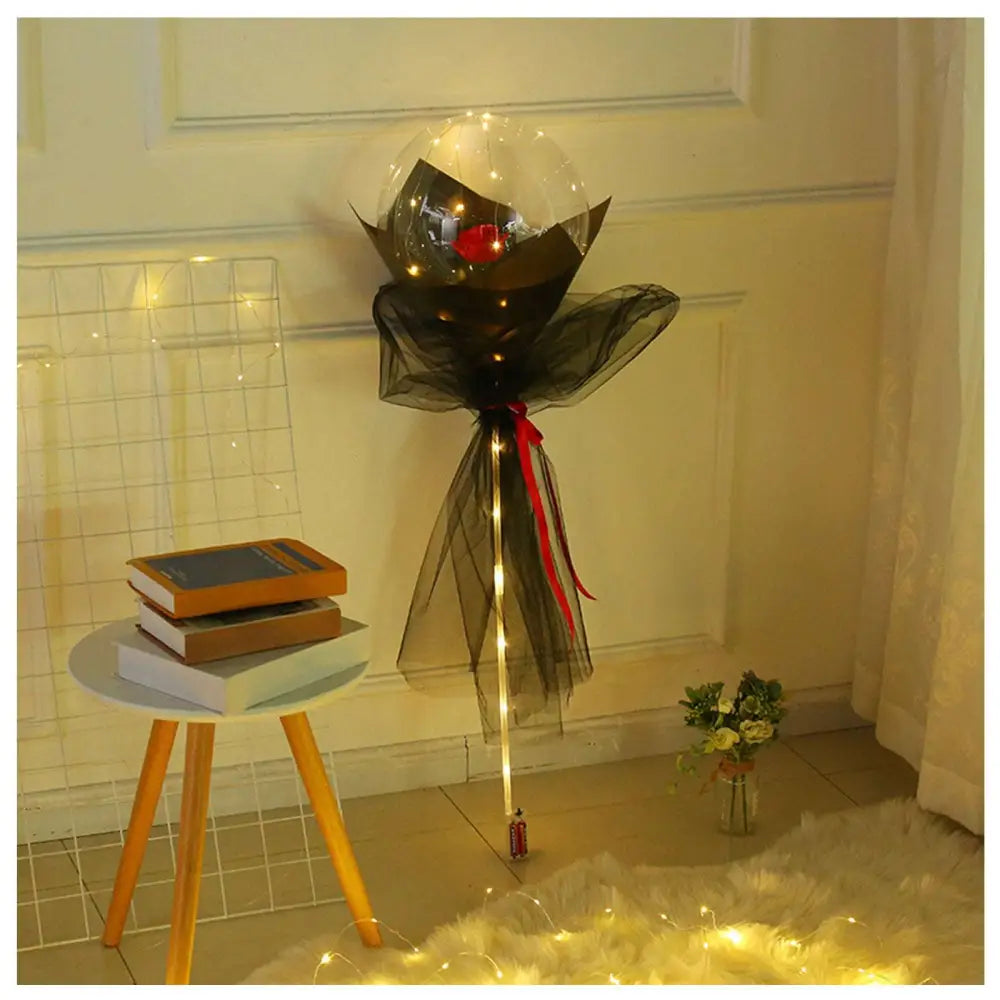 A luminous balloon rose bouquet with a red rose inside a transparent bobo ball wrapped in black sheer fabric with lights
