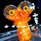 A glowing orange tulle-wrapped balloon rose bouquet with two transparent bobo balls containing illuminated sunflowers