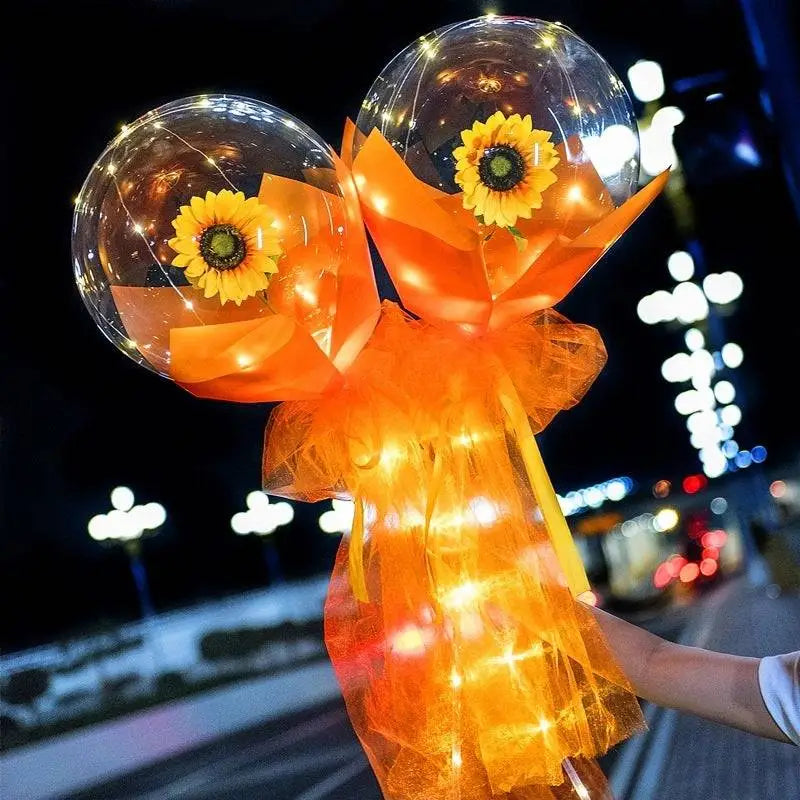 A glowing orange tulle-wrapped balloon rose bouquet with two transparent bobo balls containing illuminated sunflowers