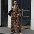A woman wears a luxurious brown and black leopard print satin two-piece suit fashion set with wide-leg pants and bell sleeves