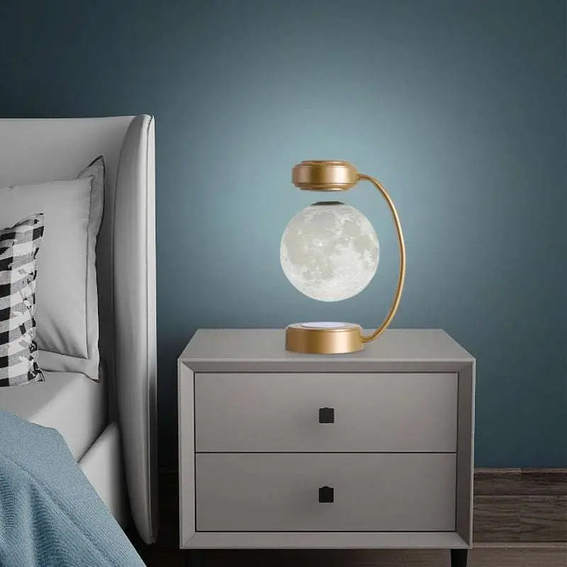 A levitating led moon night light with a gold-toned magnetic base and curved stand for wireless use