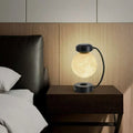 A glowing translucent levitating led moon night light with a black magnetic base and curved stand for wireless use