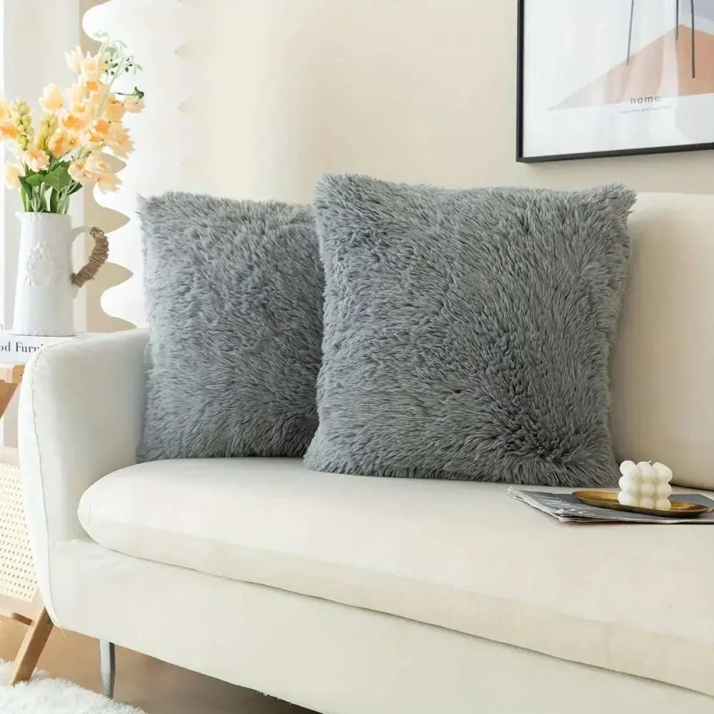 Two luxurious soft faux fur throw pillow covers in gray with a fluffy texture resting on a couch