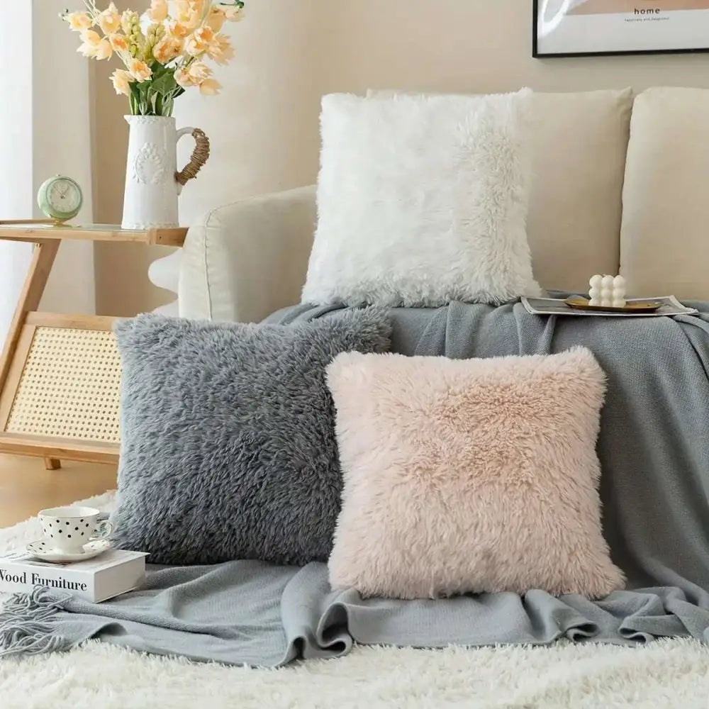 Three luxurious soft faux fur throw pillow cushion covers in gray blush pink and white on a cozy sofa