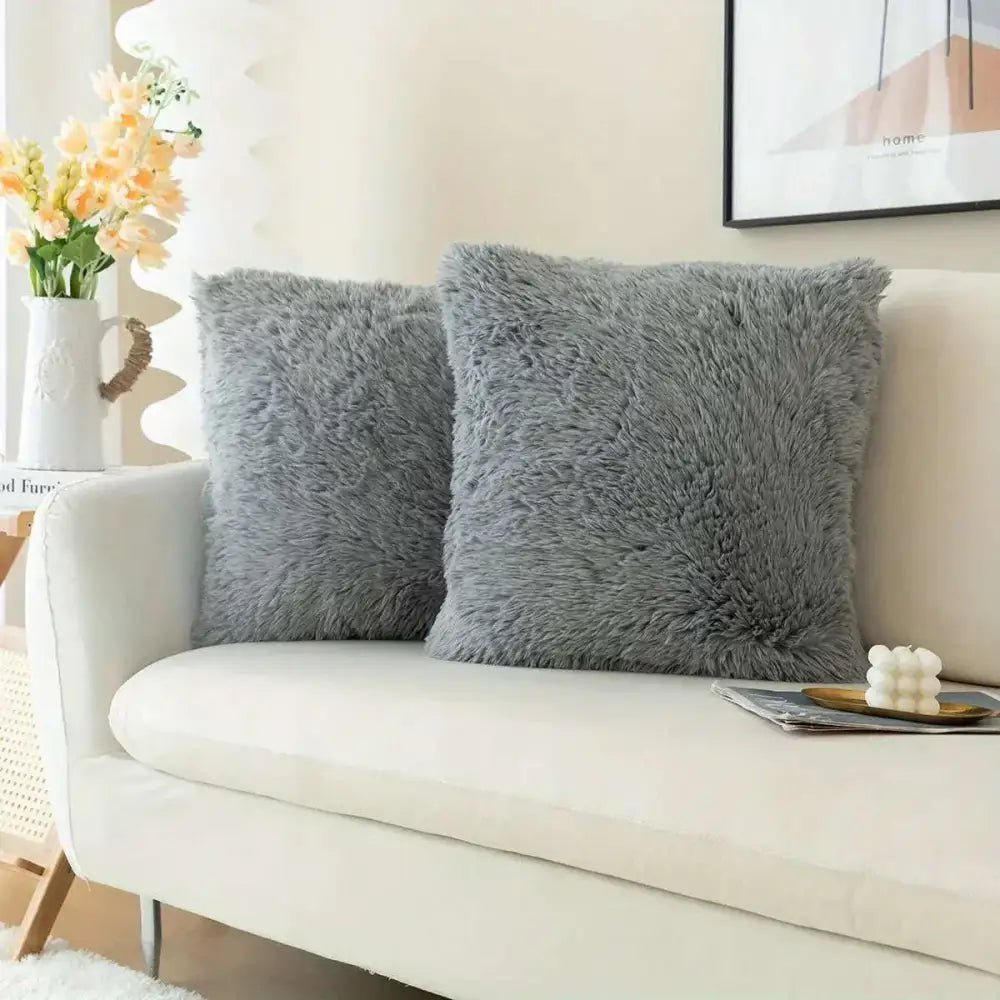 Two plush gray luxurious soft faux fur throw pillow cushion covers with a fluffy texture on a white sofa