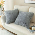 Two plush gray luxurious soft faux fur throw pillow cushion covers with a fluffy texture on a cream sofa