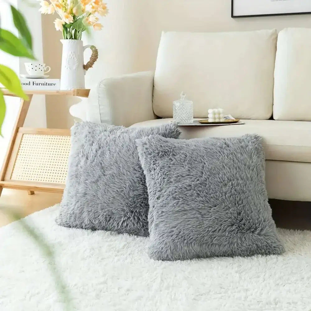 Two plush gray luxurious soft faux fur throw pillow cushion covers on a white rug showcasing their fluffy texture