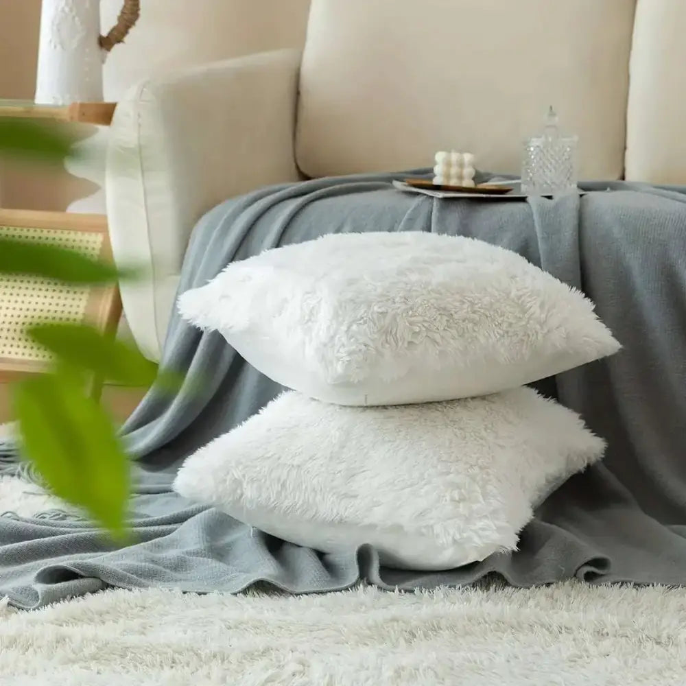 Two plush white luxurious soft faux fur throw pillow cushion covers stacked on gray blanket for cozy decor