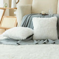 White fluffy luxurious soft faux fur throw pillow cushion covers resting on a soft gray blanket for decor