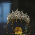 A sparkling silver forehead crown with intricate crystal and pearl rhinestone embellishments on a gold stand