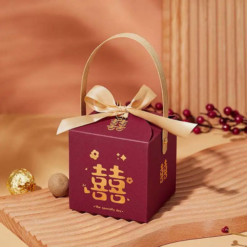 A maroon minimalist wedding candy gift box with gold double happiness characters, gold ribbon bow, and handle