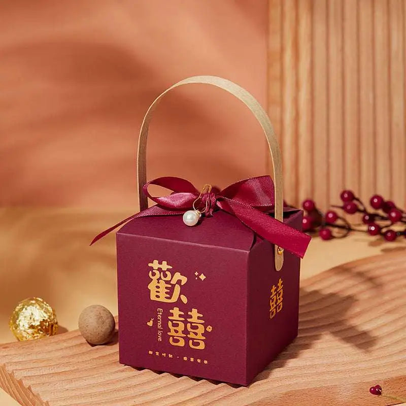 A maroon minimalist wedding candy gift box with gold chinese characters, matching ribbon bow, and pearl charm handle