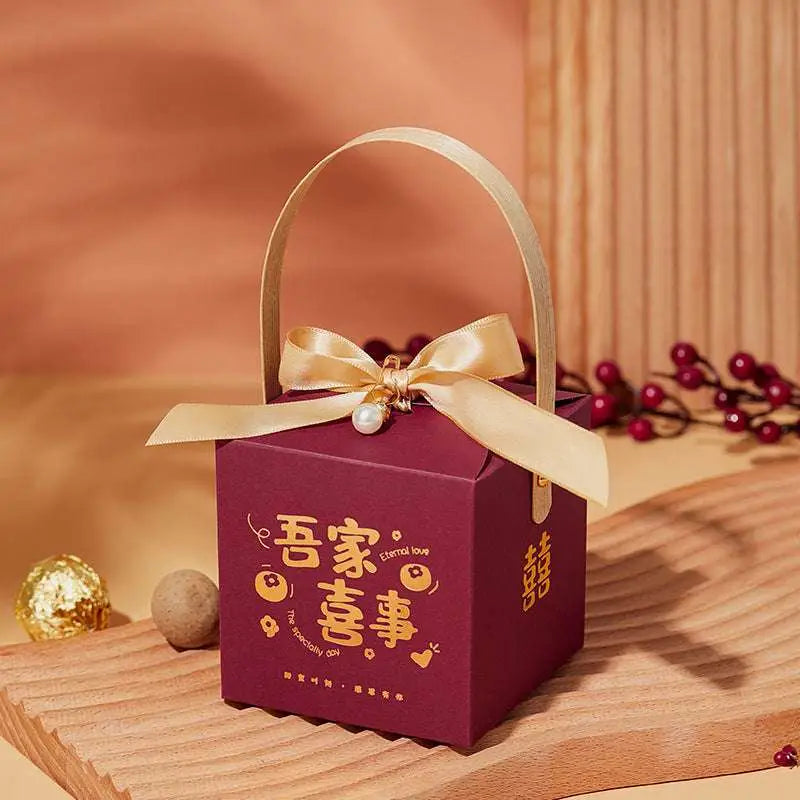 Maroon minimalist wedding candy gift box with gold foil lettering, satin ribbon bow, pearl, and gold handle