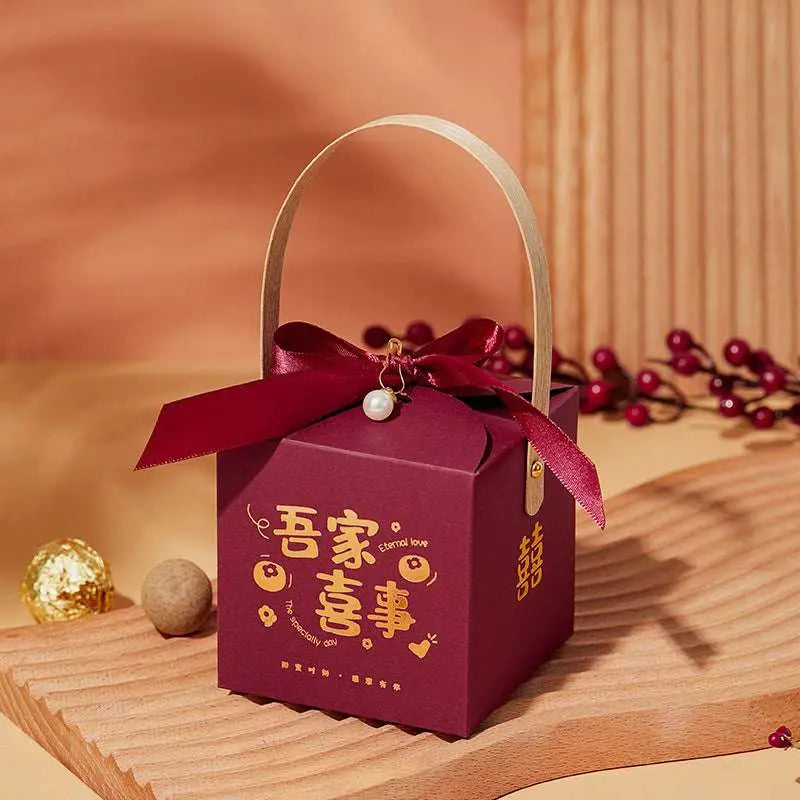 A maroon minimalist wedding candy gift box with gold foil handle, matching ribbon bow, and pearl charm detail