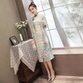 A woman wears a light mint green medium length cheongsam floral dress with teal frog closures and subtle patterned panels