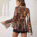 A woman wears a black mesh printed knotted flare sleeve floral romper with long bell sleeves and intricate floral pattern