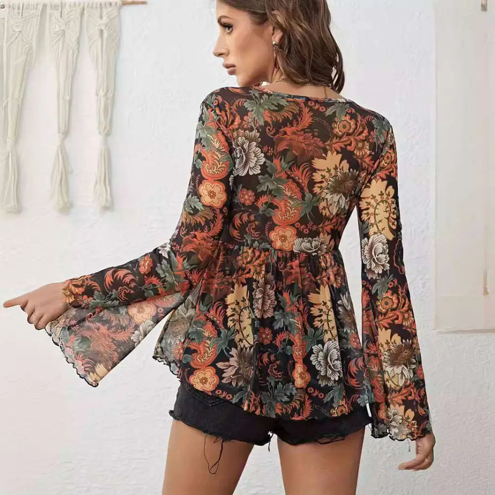 A woman wears a black mesh printed knotted flare sleeve floral romper with long bell sleeves and intricate floral pattern