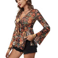 A flowing long-sleeved mesh printed knotted flare sleeve floral romper in dark base with vibrant orange and green patterns