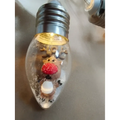 A clear glass christmas led string light bulb ornament with a miniature reindeer and faux snow in a decorative lights set