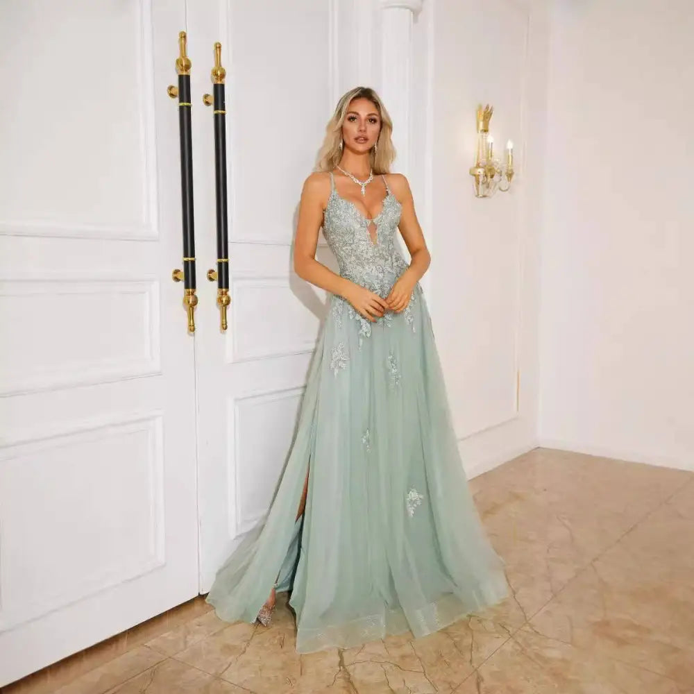A woman wears a mint green lace floor-length evening dress with floral embroidery and a high slit