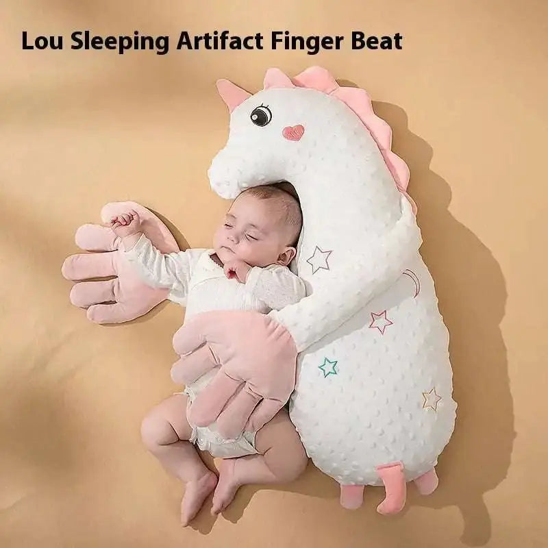A plush white unicorn sleeping aid with pink accents and star moon embroidery shown alongside a mint green plush dinosaur baby pillow